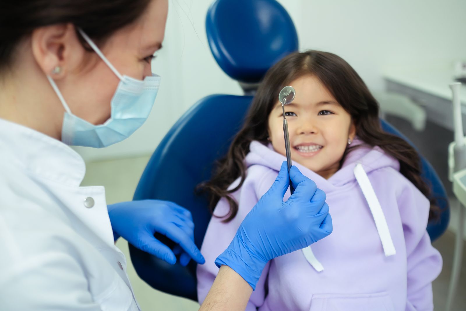 A child smiling in the chair as a dentist shows her a small mirror
