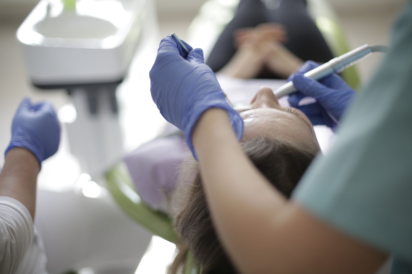 A gloved hand holding a dental mirror and handpiece over a patient